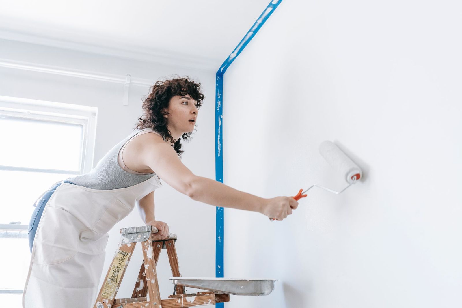 Frau auf der Leiter streicht eine Wand weiß