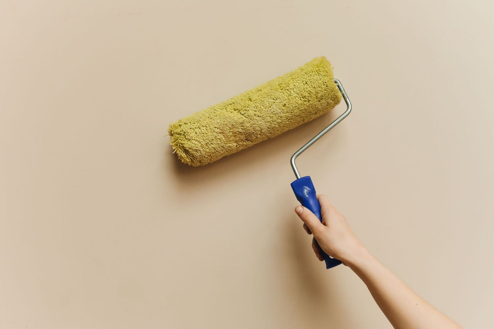 Hand mit gelber Farbrolle streicht eine beige Wand
